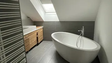 Modernes Badezimmer im Dachgeschoss mit freistehender Badewanne, Dachfenster und Holzelementen.