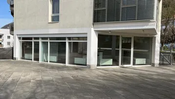 Moderne Geschäftsfassade mit großen Schaufenstern im Erdgeschoss und gepflastertem Vorplatz.