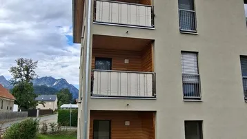 Modernes Mehrfamilienhaus mit mehreren Balkonen und Blick auf die umliegende Landschaft und Berge.