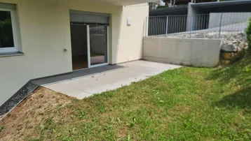 Gepflasterte Terrasse im Erdgeschoss mit angrenzender Rasenfläche und Zugang zum Innenbereich.