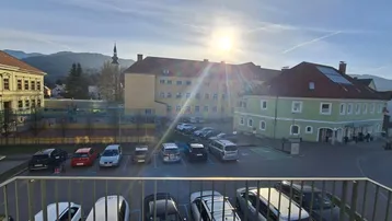 Sonniger Ausblick vom Balkon auf die umliegende Bebauung und Berge im Hintergrund.