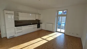 Offene Küche mit weißen Schränken, dunkler Arbeitsplatte und Holzfußboden, angrenzend an den Wohnbereich.