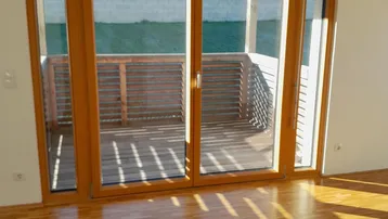 Helles Zimmer mit Holzboden und Zugang zu einem sonnigen Balkon, der viel Tageslicht hereinlässt.