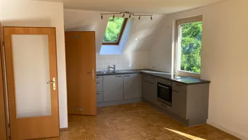 Helle Dachgeschosswohnung mit integrierter Küchenzeile, Parkettboden und Blick ins Grüne durch das Fenster.