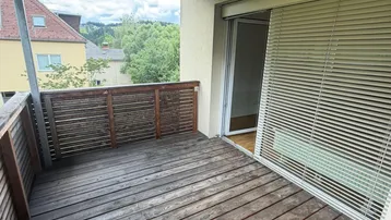 Überdachter Balkon mit Holzboden und Blick auf die umliegende Wohngegend und grüne Hügel.