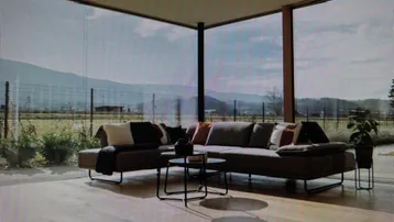 Helles Wohnzimmer mit großem Sofa und raumhohen Fenstern mit Blick auf die Berge und Landschaft.