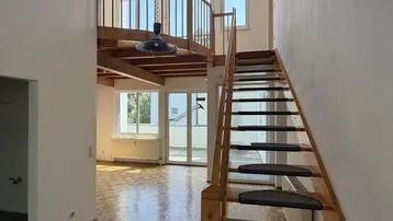 Heller Wohnbereich mit Holztreppe, Galerie und sichtbaren Deckenbalken, ausgestattet mit Parkettboden.