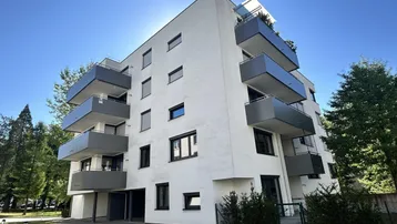 Modernes Mehrfamilienhaus mit weißer Fassade und mehreren Balkonen unter blauem Himmel.