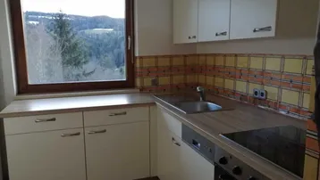 Küche mit weißen Einbauschränken, Holz-Arbeitsplatte und einem Fenster mit weitem Ausblick.