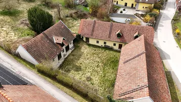 Luftaufnahme von mehreren ländlichen Gebäuden mit roten Ziegeldächern und einem großen, ungepflegten Rasenbereich.