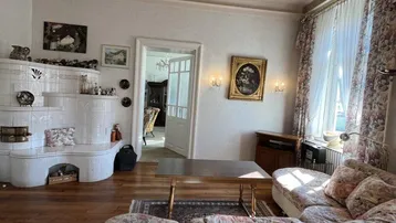 Gemütliches Wohnzimmer mit traditionellem Kachelofen, floralem Sofa und Holzboden.
