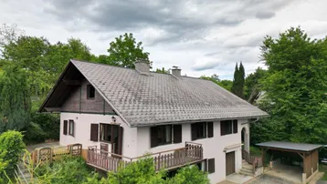 Freistehendes Haus mit Satteldach, Balkon und Carport, umgeben von viel Grün und Bäumen.