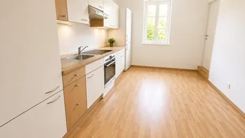 Helle Einbauküche mit Laminatboden, Holztheke und Fenster, die viel Tageslicht hereinlässt.