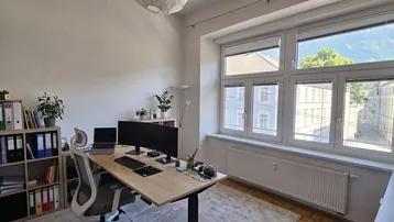 Helles Büro mit großem Fenster, das einen Blick auf die Stadt und grüne Bäume bietet, ausgestattet mit modernen Möbeln.