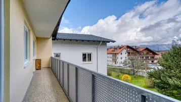 Langer Balkon mit Metallgeländer und Blick auf die umliegende Bebauung und Natur.