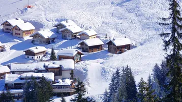 Malerisches Bergdorf mit verschneiten Chalets und Skipisten in den Alpen.