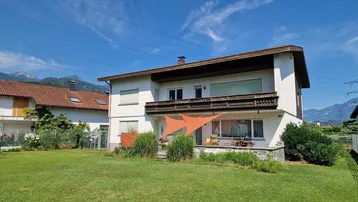 Großzügiger Gartenbereich mit Rasenfläche, Terrasse und Blick auf die umliegende Berglandschaft.
