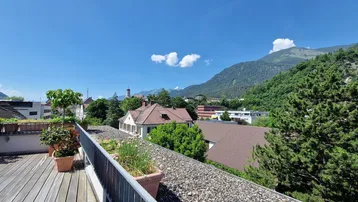 Geräumige Dachterrasse mit Holzboden, vielen Pflanzen und einem atemberaubenden Blick auf die Berge und die Stadt.