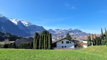 Blick auf Wohnhäuser mit schneebedeckten Bergen im Hintergrund unter klarem blauem Himmel.