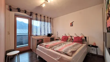 Schlafzimmer mit Doppelbett, dunklem Laminatboden und direktem Zugang zum Balkon.