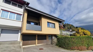 Ansicht der Hausfassade mit Garagen und Zugang zum Eingangsbereich, umgeben von Grün.