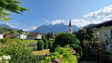 Malerischer Ausblick auf die Berge und ein Dorf mit Kirchturm, umgeben von üppigem Grün.