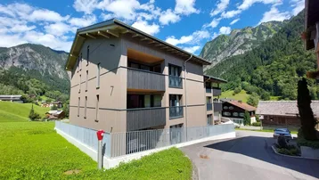 Modernes Mehrfamilienhaus mit Balkonen und Holzfassade, eingebettet in eine grüne Berglandschaft.