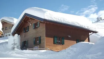 Traditionelles Holzchalet mit verschneitem Dach und Hirschgeweih an der Fassade.