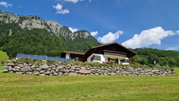 Traditionelles Haus in den Bergen mit Photovoltaikanlage und weitem Blick auf die Landschaft.