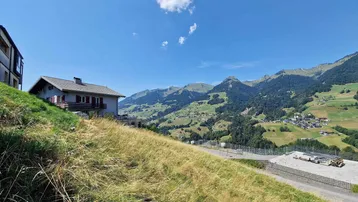 Haus auf einem Hügel mit weitem Blick auf die umliegende Berglandschaft und das Tal unter blauem Himmel.