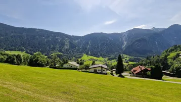 Weitläufige grüne Landschaft mit mehreren Häusern und majestätischen Bergen im Hintergrund.
