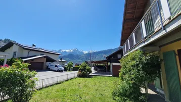 Sonniger Gartenbereich mit Rasen, Carport und beeindruckendem Bergblick in der Ferne.
