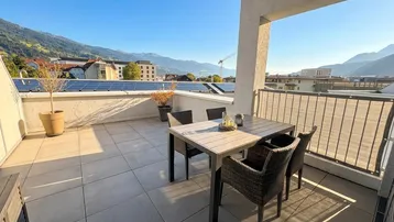 Sonnige Terrasse mit Essbereich und weitem Blick auf die umliegende Berglandschaft.