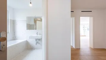 Eingangsbereich zu einem modernen Badezimmer mit Badewanne und hellen Fliesen.