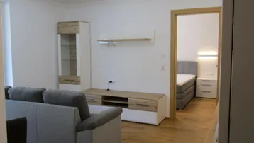 Heller Wohnbereich mit Sofa, Mediamöbeln und Blick auf das angrenzende Schlafzimmer.