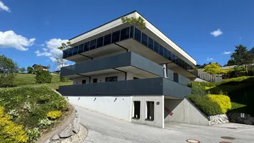 Modernes Mehrfamilienhaus mit mehreren Balkonen und Tiefgaragenzufahrt in Hanglage.