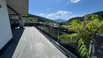 Langer Balkon mit Fliesenboden und Glasgeländer bietet einen weiten Blick auf das Tal und die Berge.