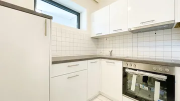Moderne Küche mit weißen Hochglanzschränken, grauen Arbeitsplatten und integriertem Backofen.