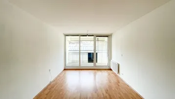 Helles Zimmer mit Parkettboden und großem Fenster, das Zugang zu einem Balkon bietet.