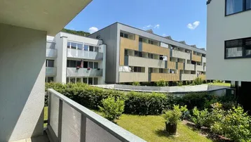 Blick vom Balkon auf den begrünten Innenhof und moderne Wohngebäude unter blauem Himmel.