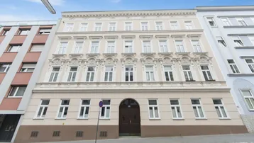 Historische Fassade eines Mehrfamilienhauses mit vielen Fenstern und dekorativen Elementen an der Straße.