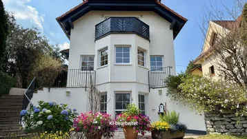 Attraktives Einfamilienhaus mit gepflegtem Vorgarten und blühenden Pflanzen unter blauem Himmel.