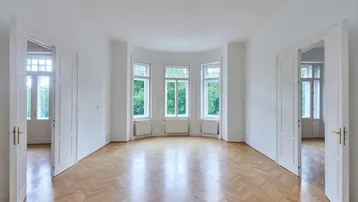 Helles, leeres Zimmer mit Fischgrätparkett und großen Fenstern mit Blick ins Grüne.