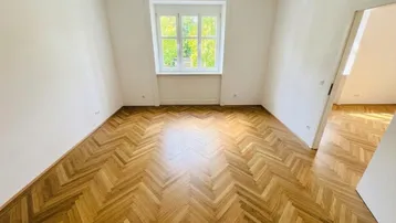 Helles Zimmer mit klassischem Fischgrätparkett und weiß gestrichenen Wänden, bereit zur individuellen Gestaltung.