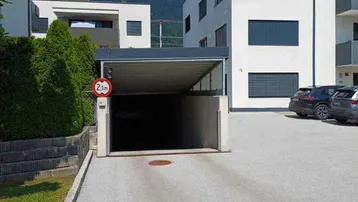 Modernes Wohngebäude mit Zufahrt zu einer Tiefgarage und Bergblick im Hintergrund.