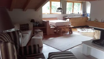 Gemütlicher offener Wohn- und Essbereich mit Holzbalkendecke, Kamin und Blick ins Grüne.
