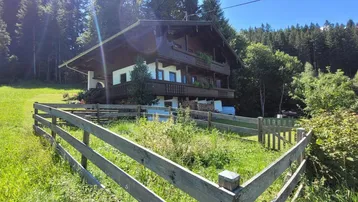 Traditionelles Holzhaus im alpinen Stil, umgeben von grünen Wiesen und Wäldern.