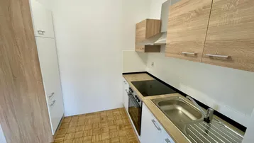 Kleine Küche mit Holzfronten, weißen Unterschränken, Einbaugeräten und Parkettboden.