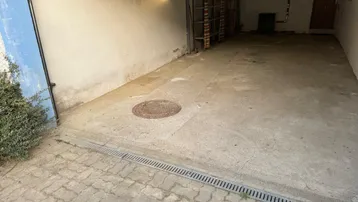 Blick in die Garage mit Betonboden, Entwässerungsrinne und gepflasterter Zufahrt.
