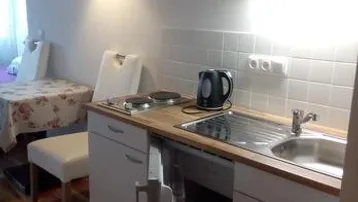 Funktionale Küchenzeile mit Spüle, Kochfeld und Holztheke, angrenzend an einen kleinen Essbereich.